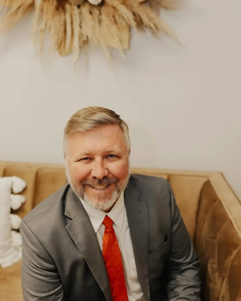 Rick Carter Jr., Ph.D., smiling in a gray suit and orange tie